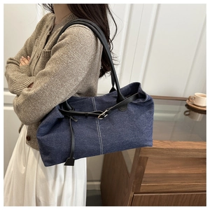 Detail of blue denim tote bag featuring black leather straps and silver buckle accents