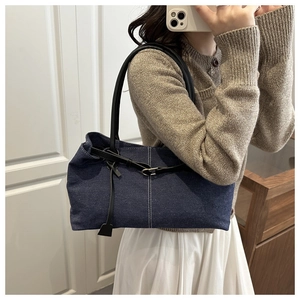 Detail of blue denim tote bag with black leather straps and white contrast stitching