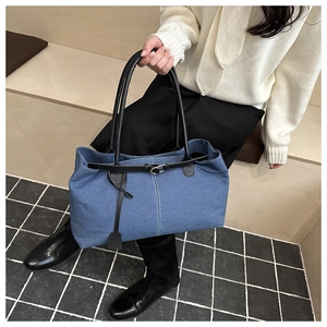 Detail of blue denim tote bag with black leather handles and white vertical stitching