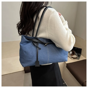 Detail of dark blue denim tote bag with white stitching and leather strap decoration