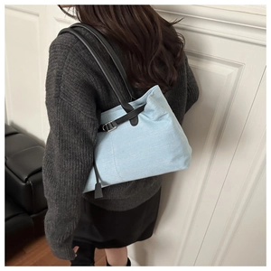 Detail view of a light blue canvas tote bag featuring black leather buckle straps