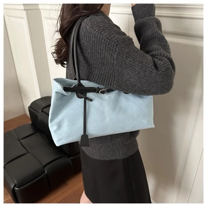 Detail of light blue denim tote bag featuring black shoulder straps and metallic hardware