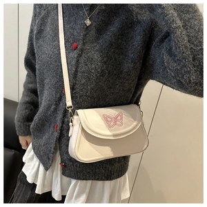 Détail du sac bandoulière crème avec broderie papillon rose porté par le mannequin