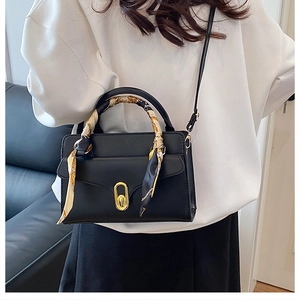 Detail of a black structured handbag featuring a gold buckle and silk scarf wrapped handle