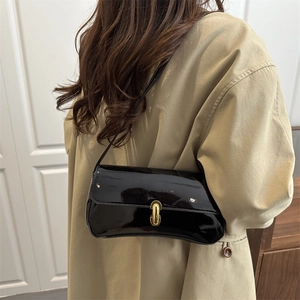 Glossy black patent leather baguette shoulder bag with gold clasp shown on a model