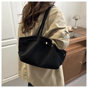 Detail of black suede tote bag with metal buckle strap shown in a real-life interior setting