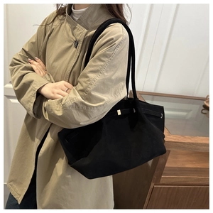Detail of black tote bag with matte finish and gold lock buckle on a female model