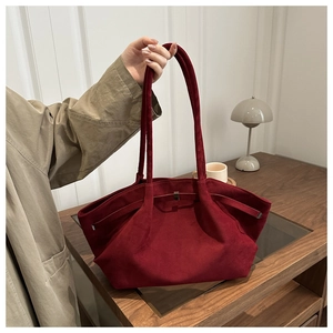 Detail view of burgundy suede shoulder bag with elegant pleats and metal buckle on wood