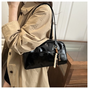 Polished black leather bowling bag with decorative wood bead charm on casual trench coat