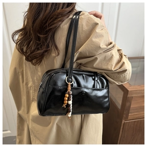 Detail of a black glossy tote bag featuring a beaded tassel charm on a model in a trench coat