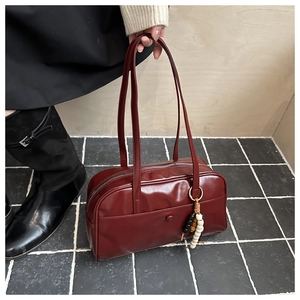 Detail of burgundy glossy tote bag with long handles and a beaded decorative charm