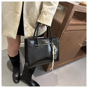 Detail of a black glossy tote bag held by a model, showing the shiny patent finish