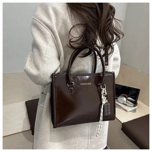 Deep brown glossy tote bag with gold lettering and chocolate charm shown on model