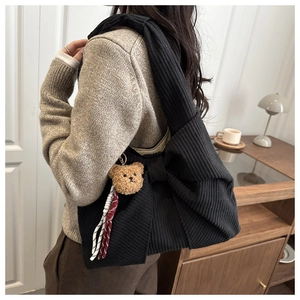 Details einer schwarzen Cord-Schultertasche mit großer Schleife und Bärenanhänger