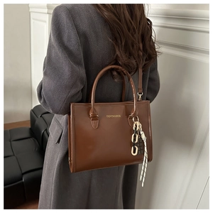 Detail of vintage brown tote bag with chain ribbon and gold brand logo on white background