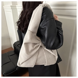 Détails de la texture du sac nœud en velours côtelé crème porté sur une veste en cuir noir