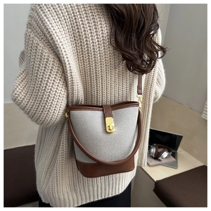 Detail of woven bucket bag with brown leather trim and golden twist-lock closure