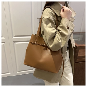 Close-up of brown leather bucket bag with gold buckle belt worn by a model