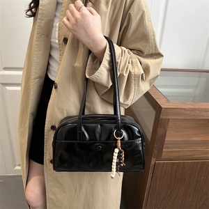 Glossy black large tote bag with bead tassel charm shown in a high-end commuter setting