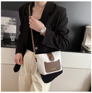 Detalle del bolso cubo bicolor con correa ajustable llevado por una modelo en ropa formal