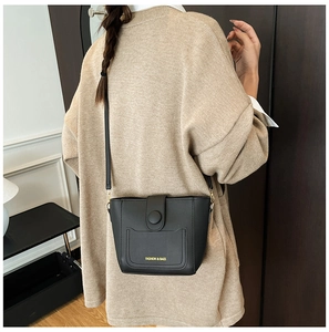 Primer plano de un bolso bombonera de cuero PU negro con letras doradas en una modelo
