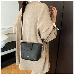 Detalle de un bolso de cubo de cuero negro combinado con un suéter de punto beige