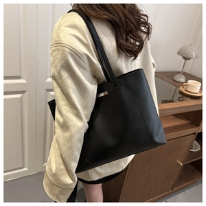 Detail of a large black leather tote bag with elegant metal clasp and embossed logo