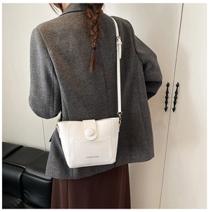 Detalle de un bolso cubo de cuero mate blanco con pespuntes y correa de hombro ajustable