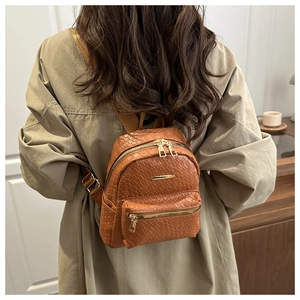 Détail de la texture tressée marron et fermeture éclair dorée sur un mini sac à dos