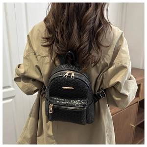Detailed view of black woven PU leather backpack on a model wearing a beige coat