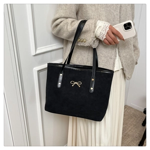 Detail of black suede tote bag featuring a gold bow accent and metallic strap rivets