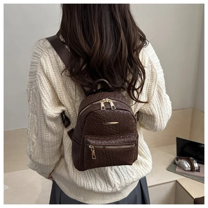 Détail d'un mini sac à dos marron foncé avec texture tressée sur un pull en maille blanc