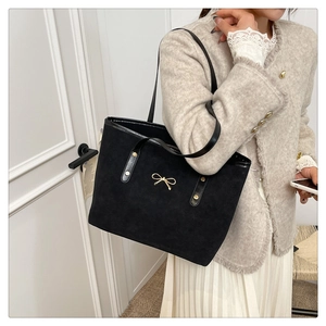 Detailed view of black suede tote bag featuring a decorative golden bow and shoulder strap