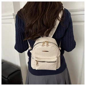 Detail of a beige woven mini backpack with gold hardware worn on a model back