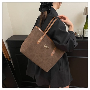 Detail of dark brown suede tote bag with leather trim and gold bow hardware