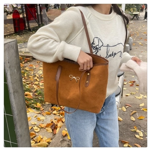 Close-up of brown suede tote bag with a gold bow buckle worn on a model's shoulder