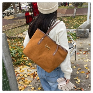 Close-up of large brown suede tote bag with golden bow detail and rivet handles