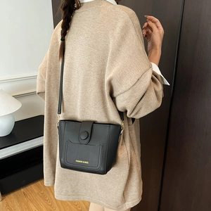 Bolso tipo cubo negro para mujer con letras doradas mostrado por una modelo con estilo