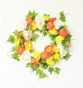 Detail of vibrant artificial summer wreath with citrus fruits and mixed flowers on wood
