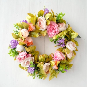 Close-up of silk pink roses and green leaves on a white wooden background wreath