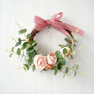 Close-up of artificial floral wreath with pink roses and striped bow on wooden wall