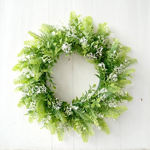 Close-up of artificial fern wreath with white flowers on white wooden background