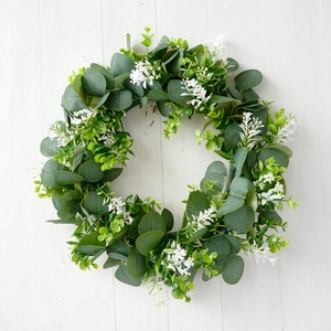 Close-up of artificial eucalyptus wreath with white flowers on white wooden background