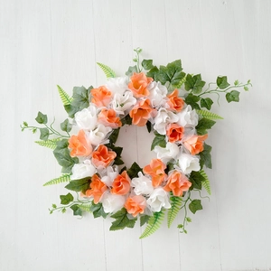 Top-down view of artificial wreath with orange roses and green ivy on white wood