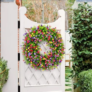 Couronne de fleurs artificielles colorées suspendue à une porte de jardin blanche