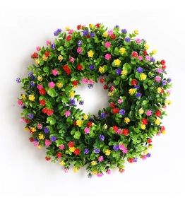 Détail d'une couronne d'eucalyptus artificielle avec petites fleurs colorées sur fond blanc