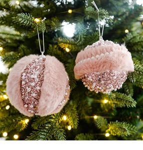 Palline di Natale rosa con pelliccia sintetica e perle appese a un ramo illuminato