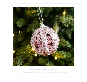 Dettaglio macro della pallina di Natale rosa con paillettes appesa a un ramo di pino