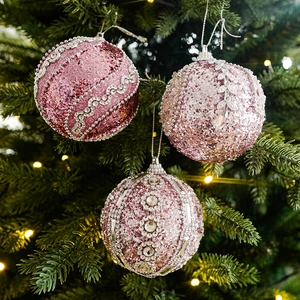 Tre palline di Natale rosa glitterate con paillettes e perle appese a un albero decorato