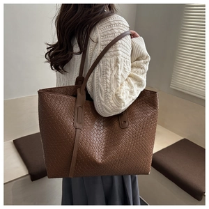 Détail du sac cabas marron tissé porté sur un pull en maille torsadée de couleur crème